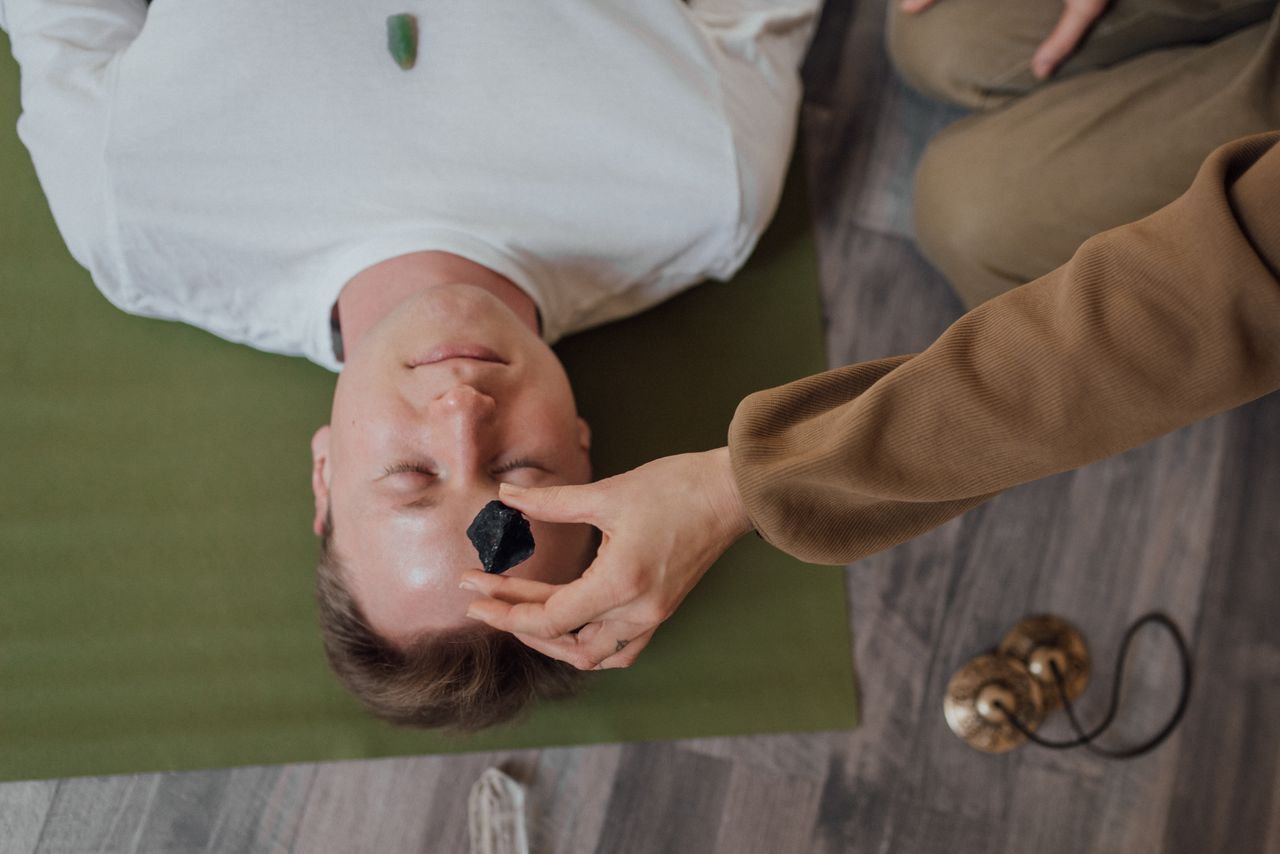 A man lying down with healing crystals placed on his forehead and chest, viewed from above.